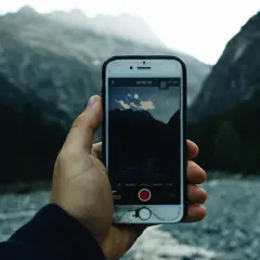 Dłoń trzyma smartfon z otwartą aplikacją do nawigacji po szlakach Tatr, na tle górskiego krajobrazu.