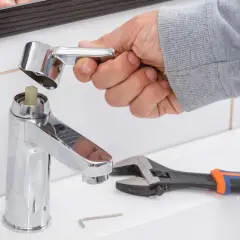 Mano desmontando grifo monomando sin tornillo. Llave inglesa y llave Allen a la vista.