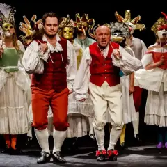 Aktorzy w barwnych strojach i maskach na scenie Teatru im. Jaracza w Warszawie.