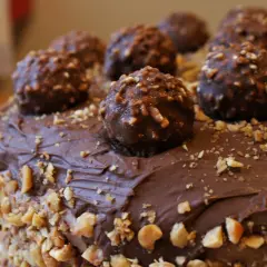 Pyszny tort oblany czekoladą, ozdobiony całymi pralinami i posypany orzechami. Wygląda jak idealny krem Ferrero Rocher.