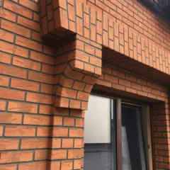 Fragment elewacji z cegły klinkierowej z ozdobnym gzymsem nad oknem.
