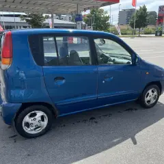 En blå Hyundai Atos står parkerad vid en bensinstation. Bilen har några rostfläckar.