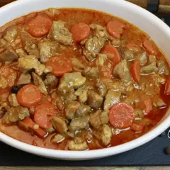 Pyszny gulasz z karkówki z marchewką w aromatycznym sosie, podany w białej misie. Obok czosnek, liść laurowy i ziele angielskie.