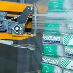 Paleta worków cementu Pegoland owinięta folią, obok maszyna pakująca.