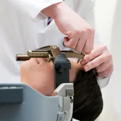 Arzt justiert stereotaktische Vorrichtung am Kopf einer Patientin. Informationen zu stereotaktische bestrahlung kosten sind hier nicht ersichtlich.
