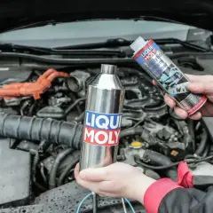 Czyszczenie katalizatora za pomocą preparatu Liqui Moly. Dwie ręce trzymają metalową butelkę i puszkę z płynem.