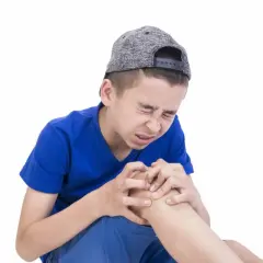 Ragazzo con cappellino grigio stringe il ginocchio con espressione sofferente, forse a causa dei dolori della crescita.