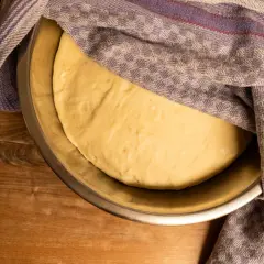 Frisch gekneteter pizzateig ruht in einer Schüssel, abgedeckt mit einem karierten Tuch.