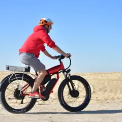 Mężczyzna w kasku i czerwonej bluzie jedzie na rowerze elektrycznym po piaszczystym terenie. Czy rower elektryczny ładuje się podczas jazdy?