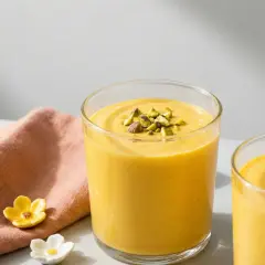 Två glas med krämig mango lassi, toppad med hackade pistagenötter. Ett perfekt recept för en svalkande dryck.