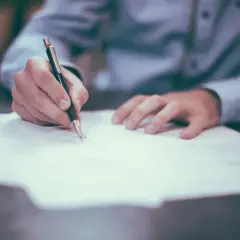 Dłoń pisze piórem na dokumencie, być może finalizując cesję.