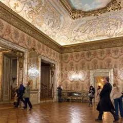 Elegancki przedpokój w pałacu z bogato zdobionym sufitem i tapetą w kwiaty. Zwiedzający podziwiają wnętrze.