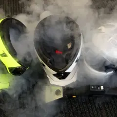 Pulire interno casco moto con vapore. Tre caschi, uno giallo fluo, uno bianco e nero, uno bianco, circondati da fumo.