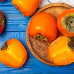 Pomarańczowe owoce kaki na niebieskim tle. Uważaj na potencjalne skutki uboczne spożycia, zwłaszcza na pusty żołądek.