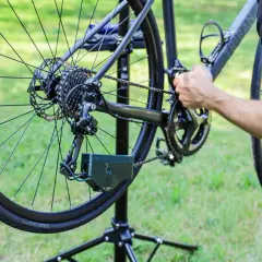 Rower na stojaku, ręka reguluje przerzutkę. Widać kasetę, łańcuch i zębatki. To część poradnika: jak zrobić napinacz łańcucha do roweru.