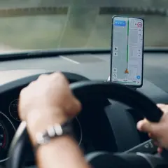 Ręce na kierownicy, przed nimi telefon z nawigacją Android pokazującą trasę i prędkość.