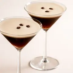 Zwei elegante Espresso Martini Gläser mit cremigem Schaum und Kaffeebohnen.