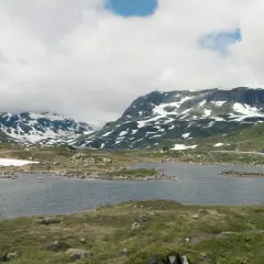 Vacker vy över Hardangervidda med snöklädda berg, en sjö och en väg. Perfekt för en vandring.