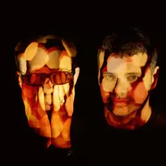 The Chemical Brothers logo is projected onto the faces of two men, one wearing sunglasses, in a dark, atmospheric setting.