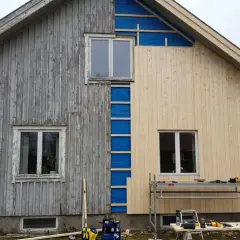 Husfasaden byts ut. Gamla träpanelen på vänster sida kontrasterar mot den nya, ljusa panelen som monteras på höger sida.