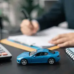 Niebieski model samochodu, kalkulator i kluczyki na biurku. Dłoń pisze na umowie, sugerując honda leasing.