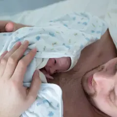 Ciepłe kangurowanie przez tatę po cesarce. Maluszek wtulony w klatkę piersiową ojca, czuje jego bicie serca.