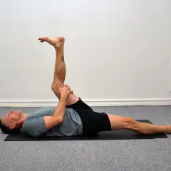 Man utför en leg curl svenska på en yogamatta, sträcker ut ena benet och böjer det andra.