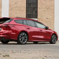 Czerwony kombi Ford Focus, elegancki i sportowy, zaparkowany przy ceglanej ścianie.