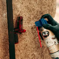 Ręka w czarnej rękawiczce aplikuje smar K2 LT-43 na metalowy element.