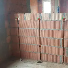 Wykonano bruzdowanie pod kable w ścianie z pustaków ceramicznych. Widać trzy pionowe bruzdy z puszkami instalacyjnymi.