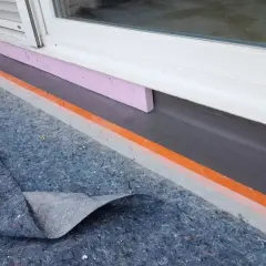 Schutzmatte liegt bereit, um den Sockel abzudichten. Dämmung und Abdichtung am Fenster sind sichtbar.