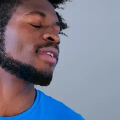 Hombre con ojos cerrados y barba cuidada, parece disfrutar de un momento de paz. Sus perillas resaltan su rostro.