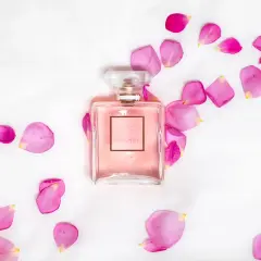 Perfumy Chanel Coco Mademoiselle w różowym flakonie otoczone płatkami róż na białym tle.