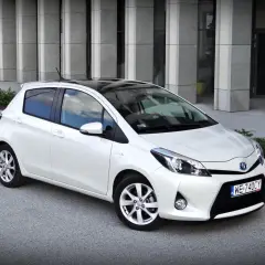 Biały Toyota Yaris z czarnym dachem, zaparkowany przed nowoczesnym budynkiem. Wiele osób szuka takich aut, czytając toyota yaris opinie.