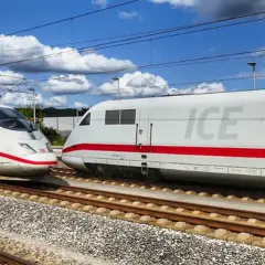 Zwei weiße ICE-Züge mit roten Streifen auf Gleisen, bereit für den Bahn Fernverkehr unter blauem Himmel mit Wolken.