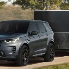 Szary Land Rover Discovery Sport z przyczepą kempingową na leśnej drodze. Idealny samochód do przyczepy kempingowej.