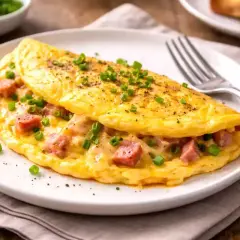 Une omelette simple et dorée, garnie de dés de jambon et de ciboule fraîche, prête à être dégustée.