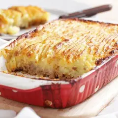 Un plat de hachis parmentier, dont l'origine remonte à Antoine-Augustin Parmentier, est servi dans un plat rouge à pois blancs.