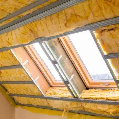 Isolation en laine de verre dans des combles aménageables, sous une structure métallique et des fenêtres de toit.