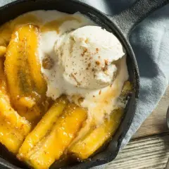 Banane flambée servie dans une poêle en fonte, nappée de glace à la vanille et saupoudrée de cannelle. Un délice gourmand.