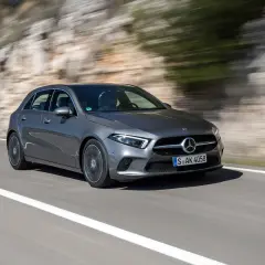 Une Mercedes-Benz Classe A grise roule sur une route de campagne, le paysage flou par la vitesse. Son moteur classe a offre une conduite dynamique.