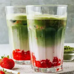 Zwei erfrischende Matcha-Erdbeer-Latte-Gläser mit Schichten aus Erdbeeren, Milch und leuchtend grünem Matcha.