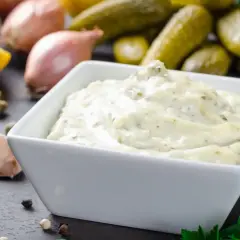 Un bol d'aïoli crémeux, prêt à être dégusté. Ingrédients frais : ail, citron, câpres, échalotes, cornichons, persil. Une recette d'aïoli simple et savoureuse.