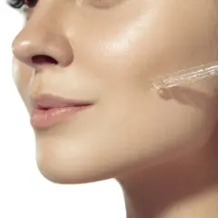 Eine Pipette gibt ein Serum auf die Wange einer Frau. Ein Tropfen mit Glykolsäure deutsch für strahlende Haut.