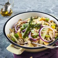 Salade de crozet colorée avec asperges, oignons rouges, pommes et dés de jambon, servie dans un plat émaillé.