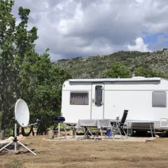 Schéma installation TV camping-car : parabole satellite devant une caravane, avec table et chaises dressées pour un repas en plein air.