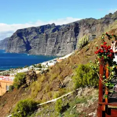 Widok na klify Los Gigantes na Teneryfie, z turystami na tarasie z kwiatami.