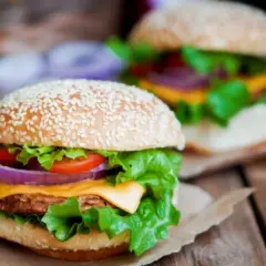 Dwa soczyste burgery z domowym fast foodem, pełne świeżych warzyw i sera, na drewnianym stole.