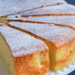 Pokrojony sernik posypany cukrem pudrem na białym talerzyku.