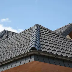 Szary dach czterospadowy z dachówki ceramicznej, z widocznym kominem i piorunochronem.